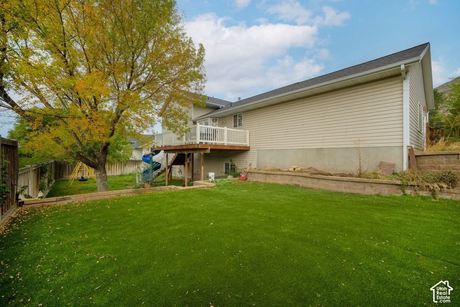 Fenced backyard lawn with a large tree, play area, and a spiral slide coming off the deck